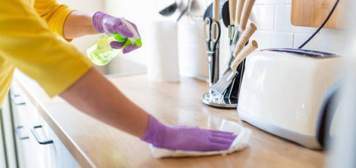 Hands in gloves disinfecting kitchen counter and wiping with paper towel against viruses